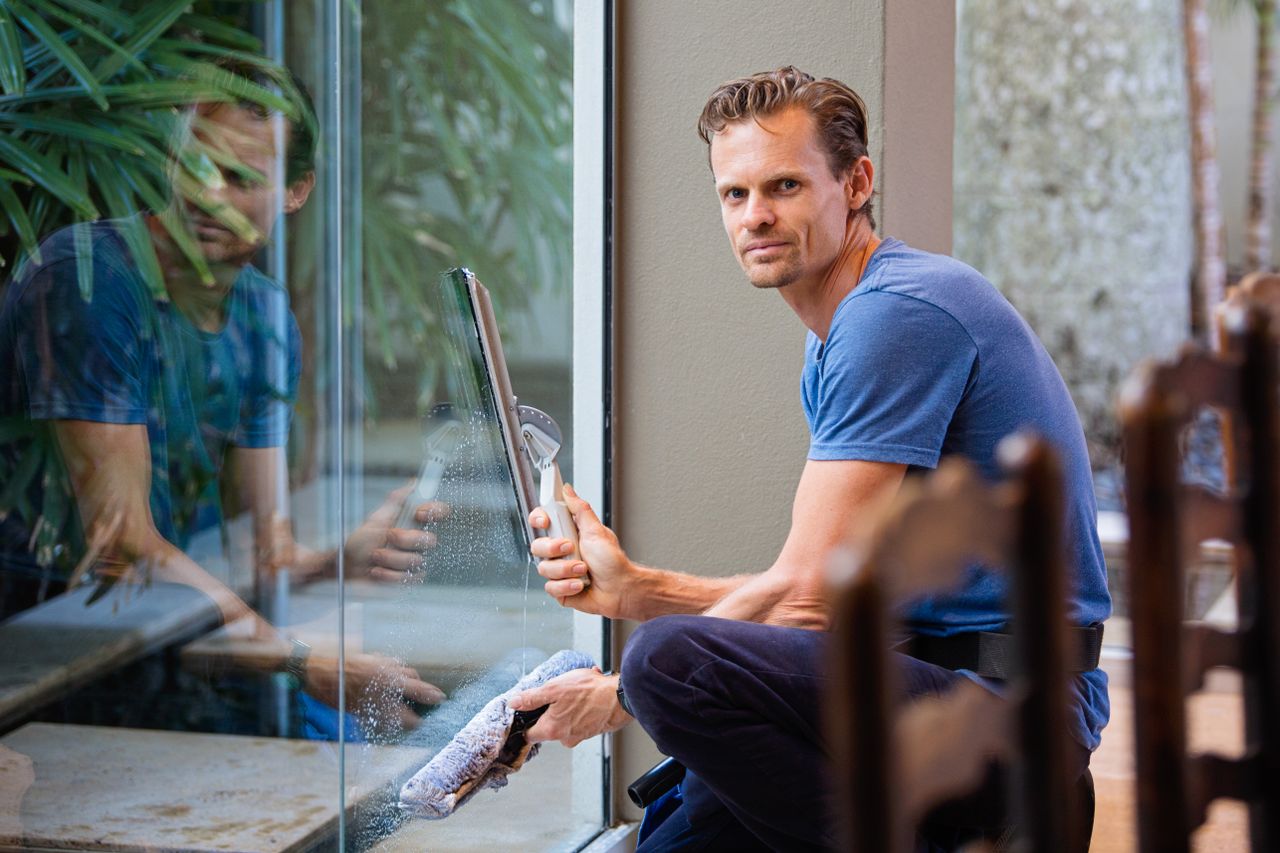 gallery-01 A man in a blue t-shirt cleaning large glass pane with a squeegee indoors.